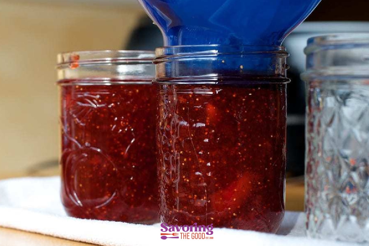 Two jars of thick strawberry jam with a blue jug.
