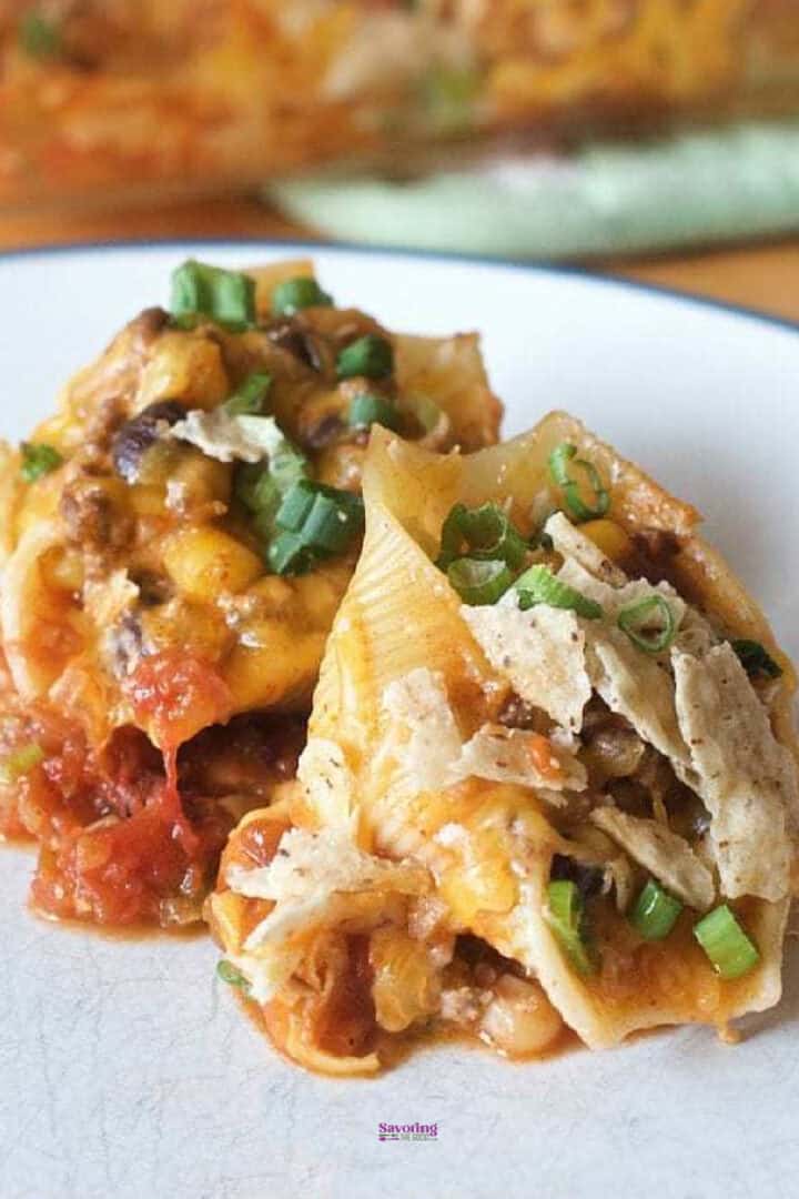 Taco stuffed shells recipe: These delicious pasta shells are filled with melted cheese, seasoned ground meat, and green onions, all served on a white plate.