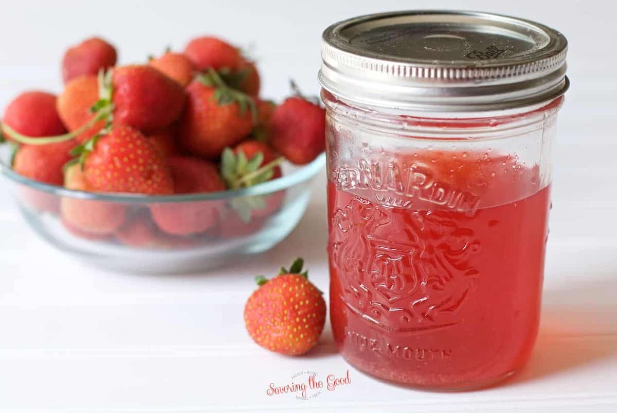 quart jar of strawberry vodka sitting on a white surface with a bowl of strawberries to the left of the jar