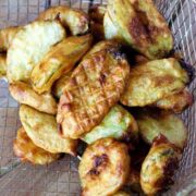 Deep Fried zucchini chips in a metal basket on a wooden table.