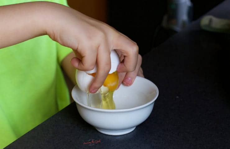 young boys hand cracking an egg into a white bowl.