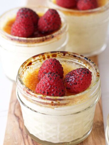 Sous Vide Creme Brulee cups on a wooden board topped with torched raspberries.
