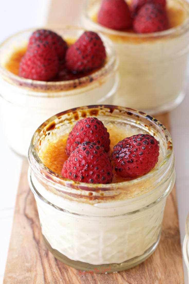 Sous Vide Creme Brulee cups on a wooden board topped with torched raspberries.