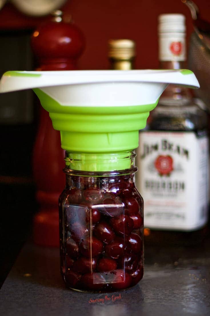 bing cherries in a canning jar with a funnel on top. Jim Beam bourbon in the background