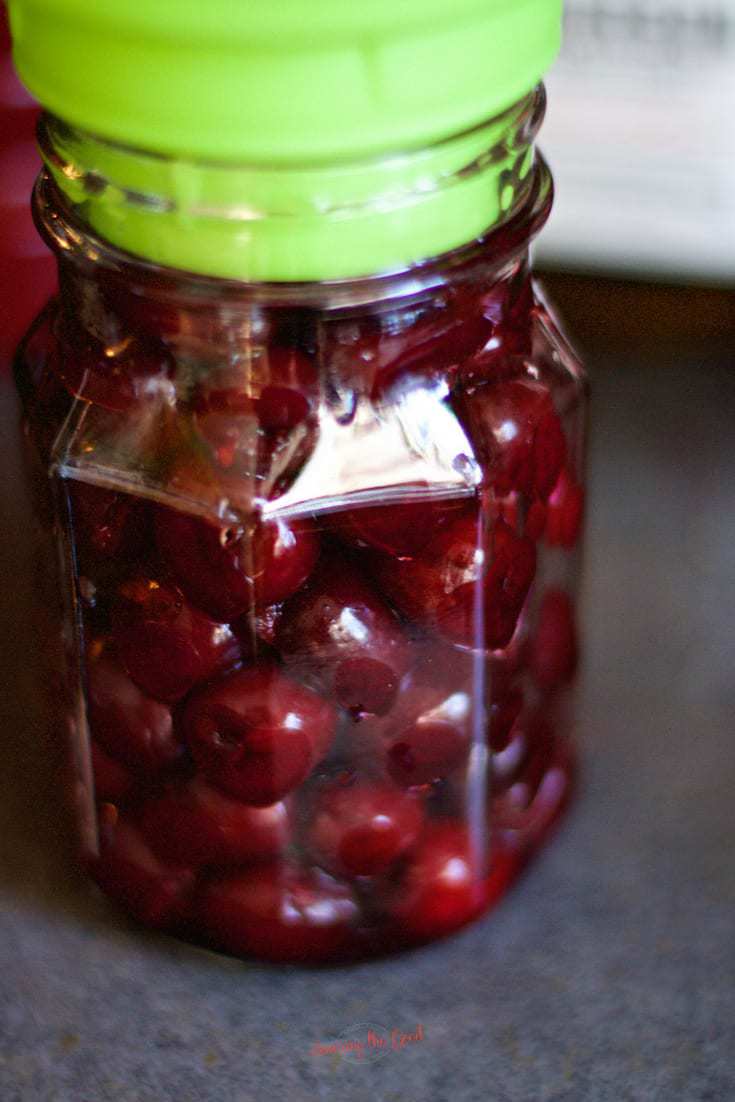 Bing cherries in a canning jar with a green funnel.