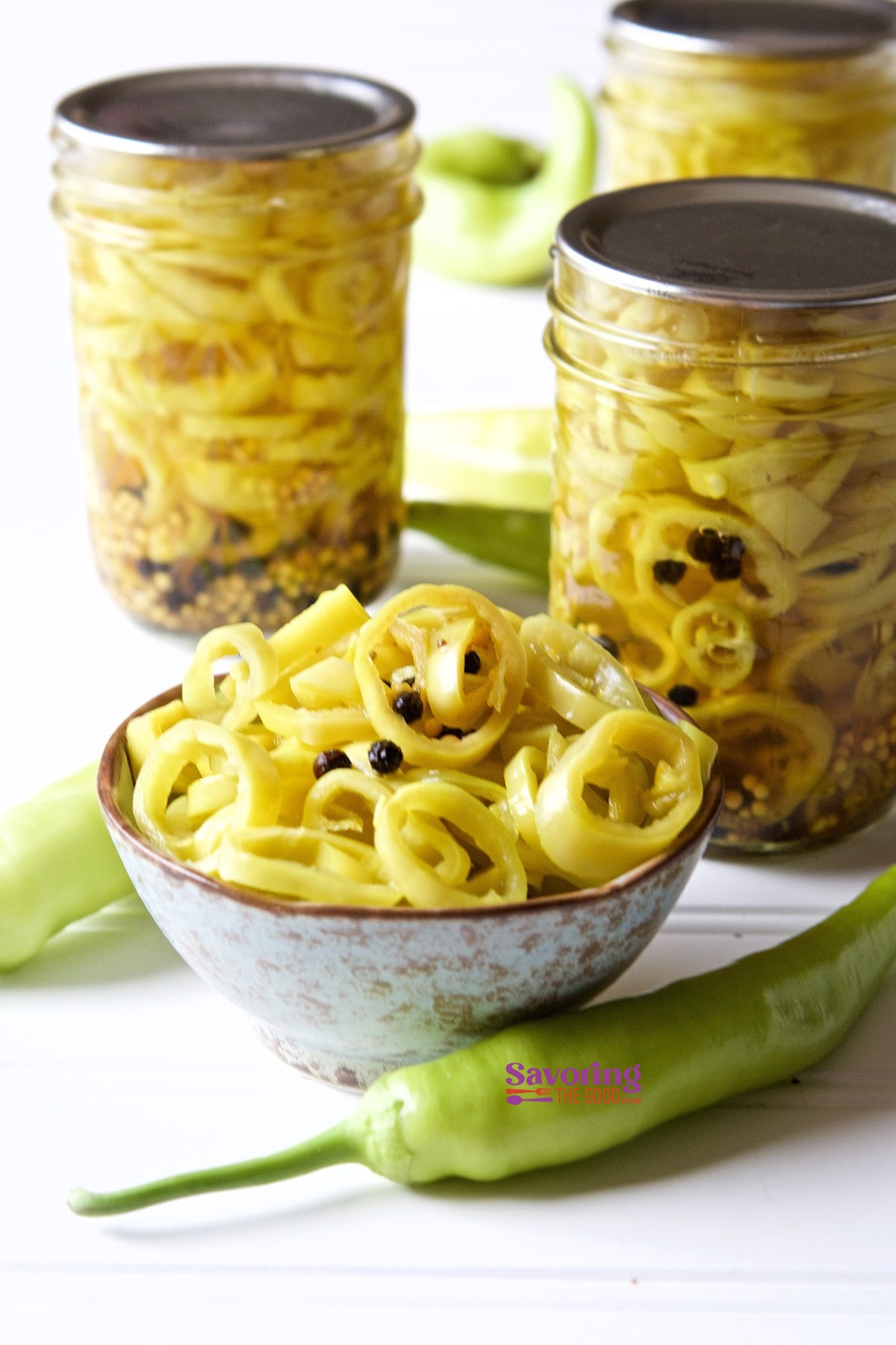 This is the easiest pickled banana peppers recipe. These are the best pickled banana peppers because they are crips, spicy and ready in hours instead of days. Canning crisp banana peppers has never been this quick or this delicious! I use the sous vide method of cooking to quickly pickle banana peppers. The lower temperature ensures the peppers retail their crunch while having the sweet banana peppers pickle in hours instead of days. I have water bath canning instructions for those of you who do not have a sous vide. #bananapeppers #pickling #canning #sousvide #sousviderecipe spicy pickled banana peppers in a bowl with multiple jars of canned banana peppers around them