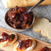 A wooden board with bread and cranberry jam, topped with tomato jam.