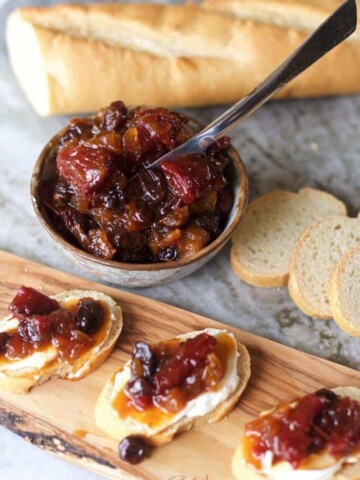 A wooden board with bread and cranberry jam, topped with tomato jam.