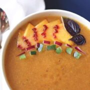 A bowl of peach gazpacho soup with a spoon on top.