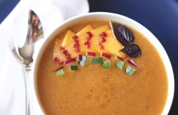 A bowl of peach gazpacho soup with a spoon on top.