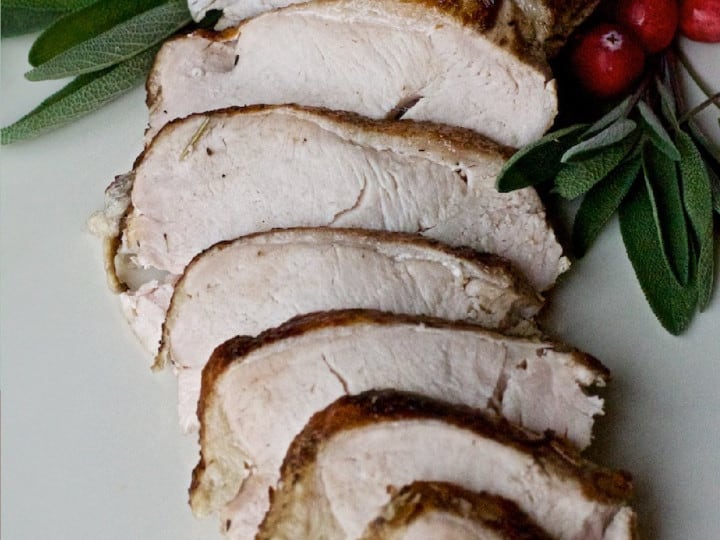Simple turkey breast recipe with cranberries and sage on a white plate.