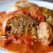 stuffed cabbage rolls on a plate with one sliced open showing the inside of one roll