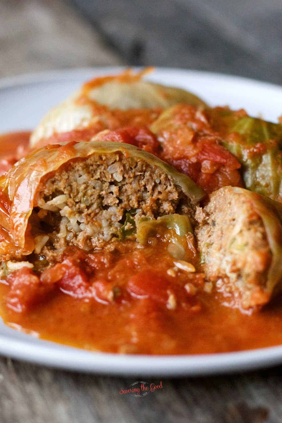 stuffed cabbage rolls on a plate with one sliced open showing the inside of one roll