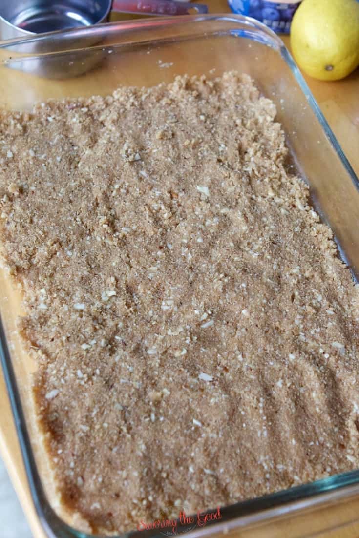 A glass baking dish filled with an even layer of crumbly brown graham cracker crust mixture, ready for baking the perfect Blueberry Delight Recipe.