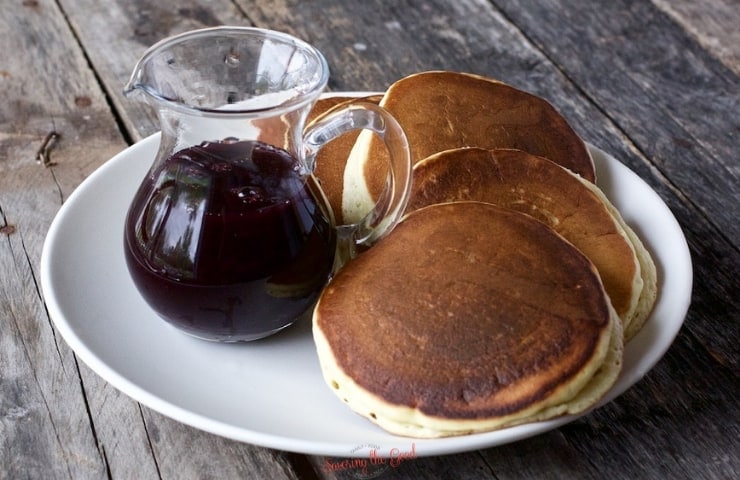 Blueberry Syrup in a jar next to a stack of pancakes, horizontal image