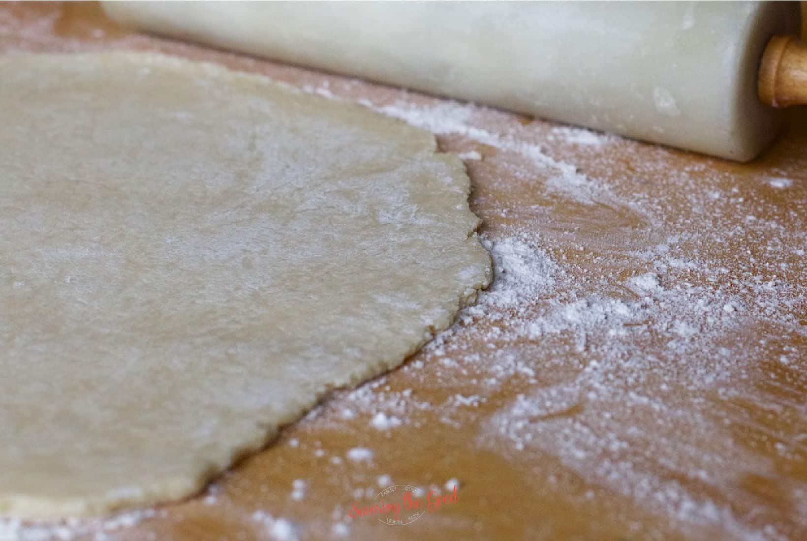 pie dough rolled out on a floured surface with a marble rolling pin to the side.