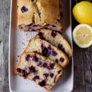 Lemon Blueberry Bread sliced on a white plate with sliced lemons for garnish