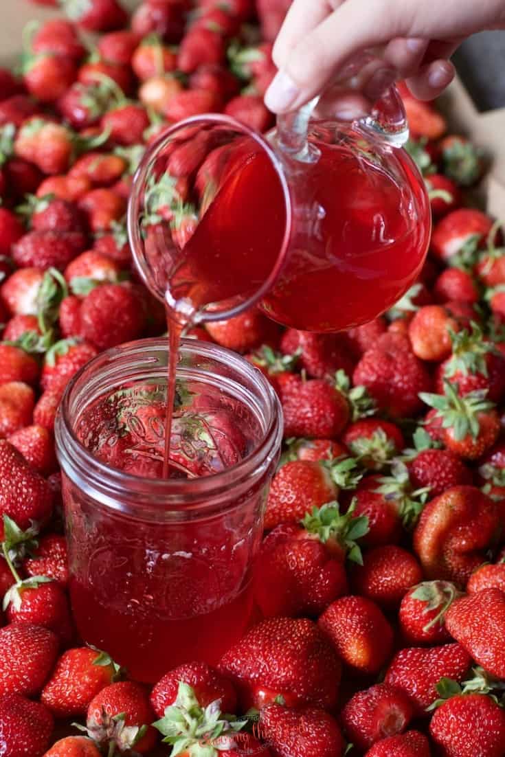 strawberry simple syrup being poured out of a clear glass pitcher