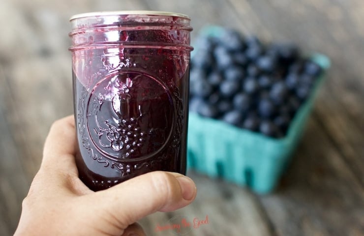 quart jar of home made blueberry syrup, horizontal image, with fresh blueberries in the background