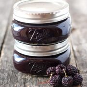Two jars of seedless blackberry jam on a wooden table.