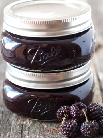Two jars of seedless blackberry jam on a wooden table.