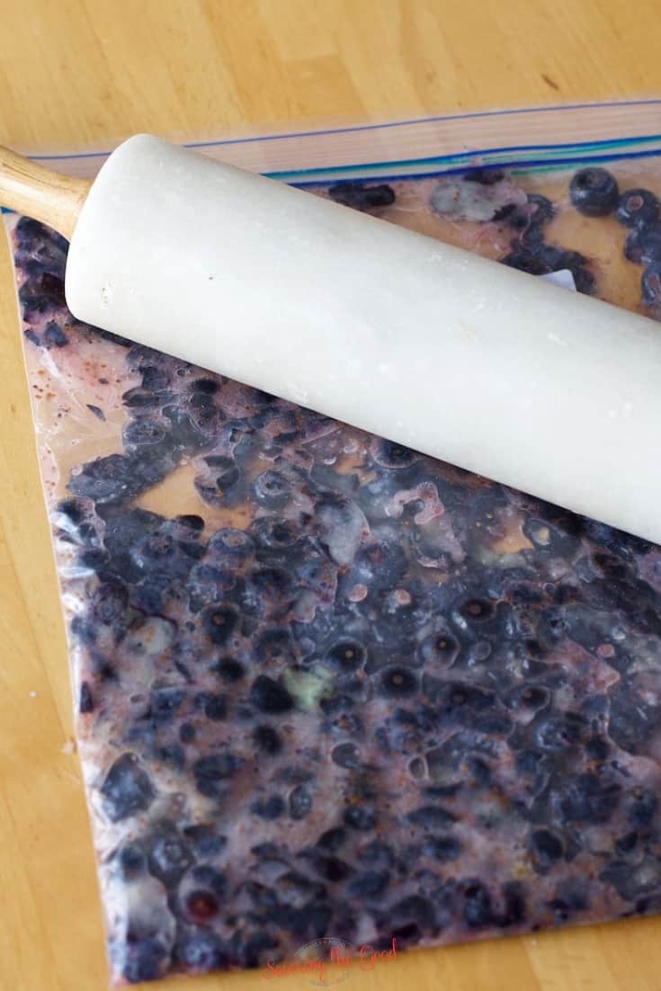 fresh blueberries in a gallon zip top bag with rolling pin crushing them