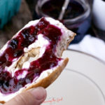 bagel with cream cheese and blueberry jam , bite taken out of it.