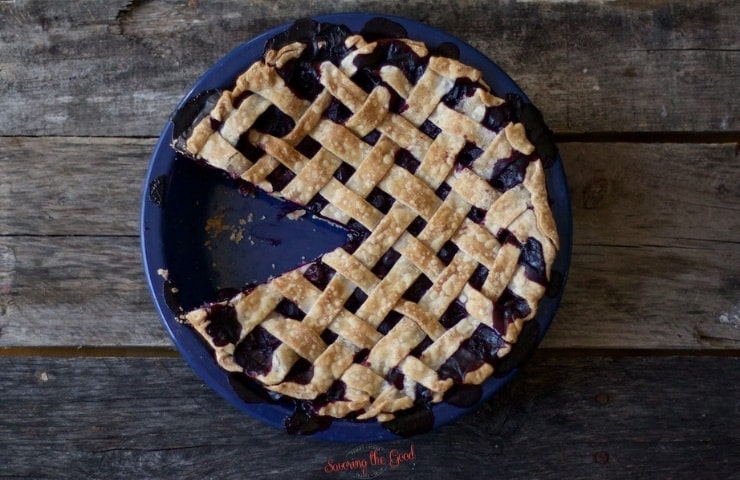 horizontal image of image of blueberry pie recipe with a piece removed on a dark rustic wood surface.