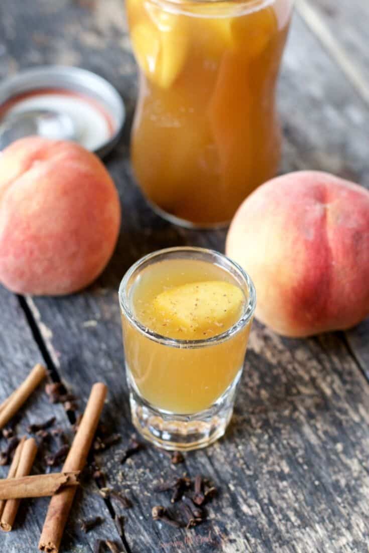 peach moonshine recipe in a glass shot glass with peach garnish and nutmeg garnish