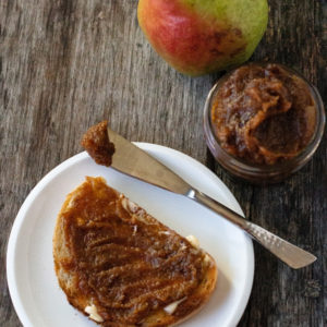 pear butter on buttered toast on a white plate with a jar and a spreading knife