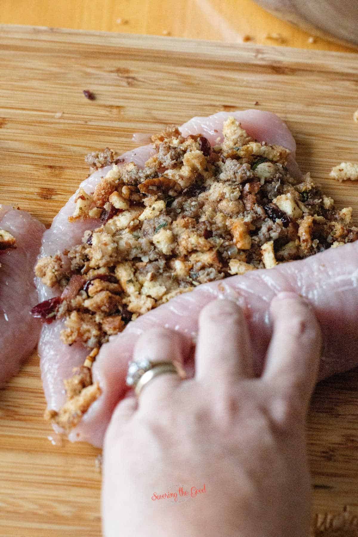 female hand rolling a flattened turkey breast stuffed with thanksgiving stuffing