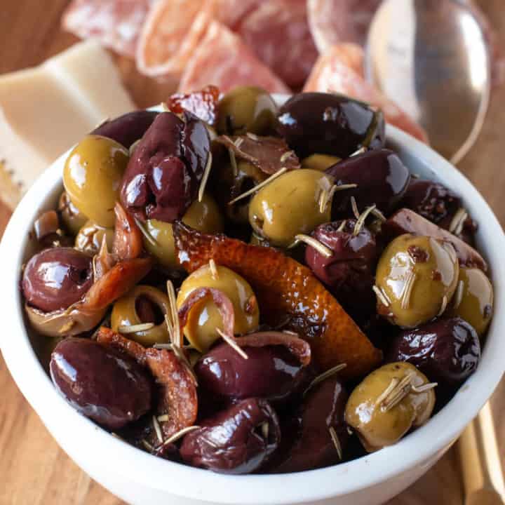 warm olives in a white bowl with cheese and meat in the background