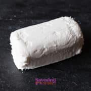 A log of white goat cheese rests on a dark slate surface, ready to be transformed into crispy fried goat cheese.