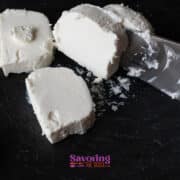 Several slices of white cheese, reminiscent of fried goat cheese, are being cut with a knife on a dark surface.