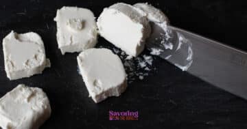 Several slices of white cheese, reminiscent of fried goat cheese, are being cut with a knife on a dark surface.