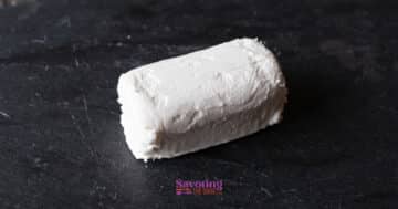 A log of white goat cheese rests on a dark slate surface, ready to be transformed into crispy fried goat cheese.