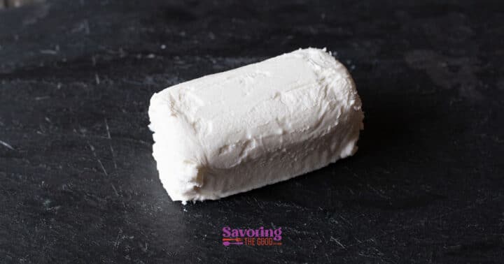 A log of white goat cheese rests on a dark slate surface, ready to be transformed into crispy fried goat cheese.