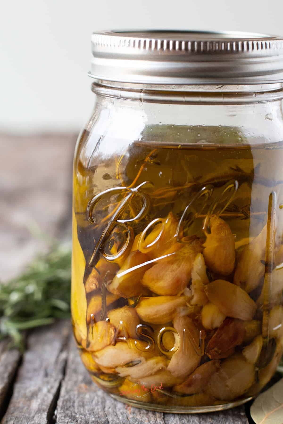 garlic confit with herbs in a ball canning jar covered in olive oil
