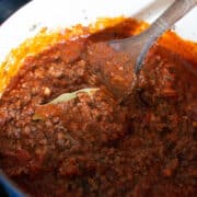 A pot of thick, chunky meat sauce with tomatoes and a bay leaf, being stirred with a wooden spoon-the perfect hearty base for Lasagna Soup.