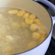 Sliced plantains boiling in water inside a white pot on a stove, resembling the preparation of gnudi with their soft and tender texture.