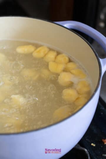 Sliced plantains boiling in water inside a white pot on a stove, resembling the preparation of gnudi with their soft and tender texture.