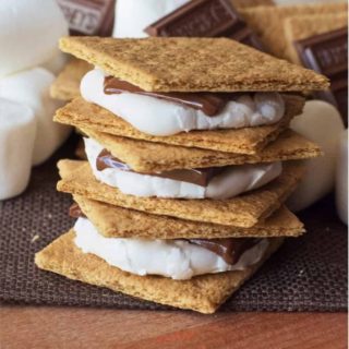 Indoor S’mores stacked on each other, 3 high with graham crackers, chocolate and marshmallows in the backgorund