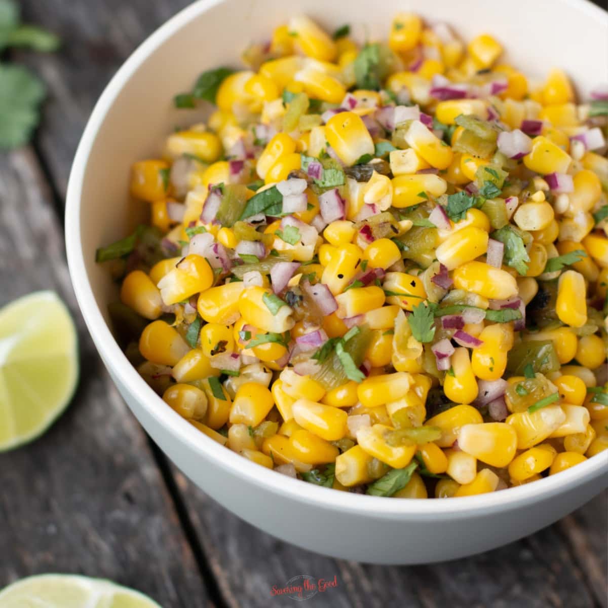 chipotle corn slasa in a white bowl showing texture of the salsa, limes in the background, square image