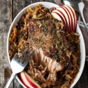 Roast pork with shredded garnish and sauerkraut in an oval dish, beautifully accented with sliced red apples.