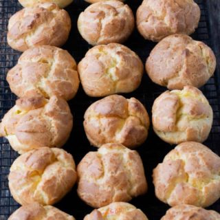 over a dozen golden brown choux pastry puffs closely spaced together on a cooling rack.