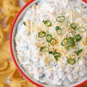 Easy Mexican Corn Dip in a red rimmed bowl with chips