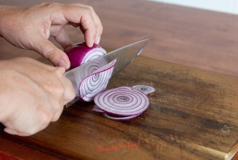 thinly slicing a red onion on a wooden cutting board