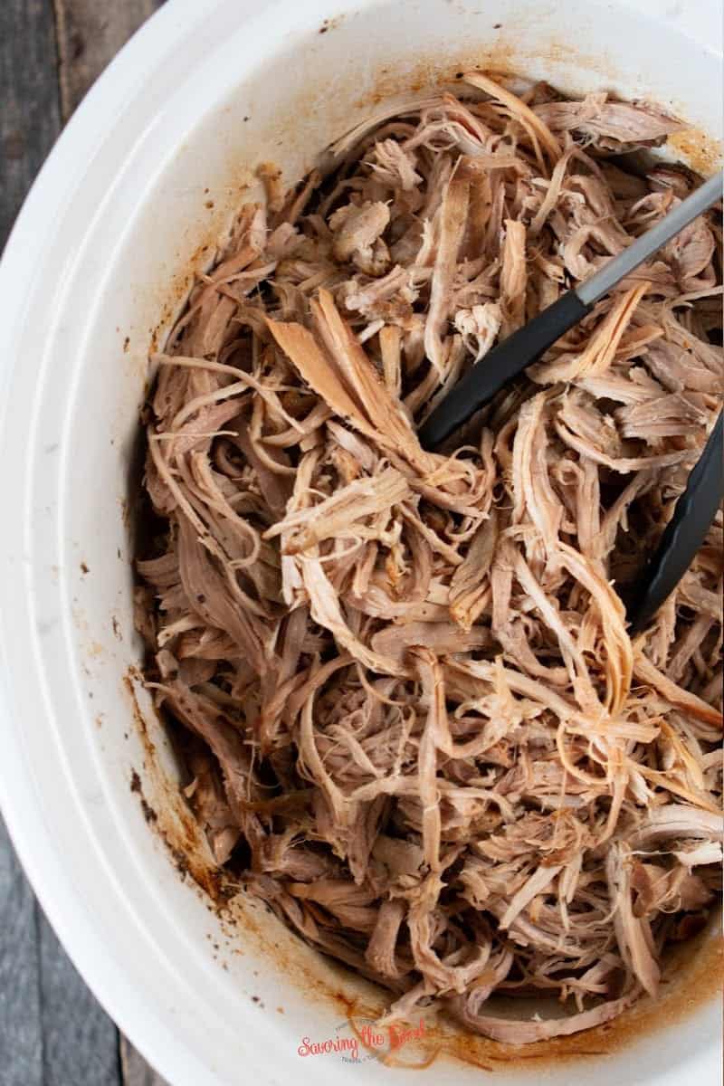 shredded pulled pork in a crock pot with tongs in the pot