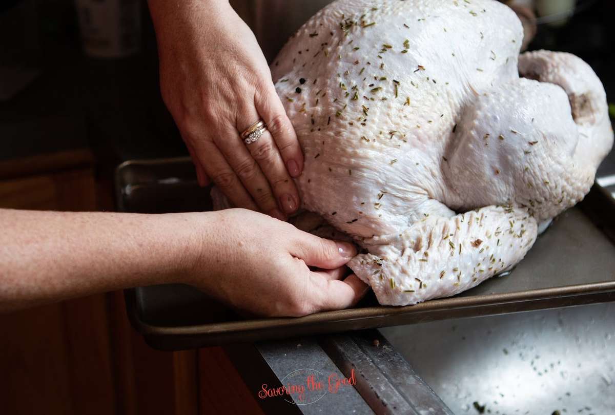 female hands tucking in the turkey wings to stabilize the turkey for smoking on the grill