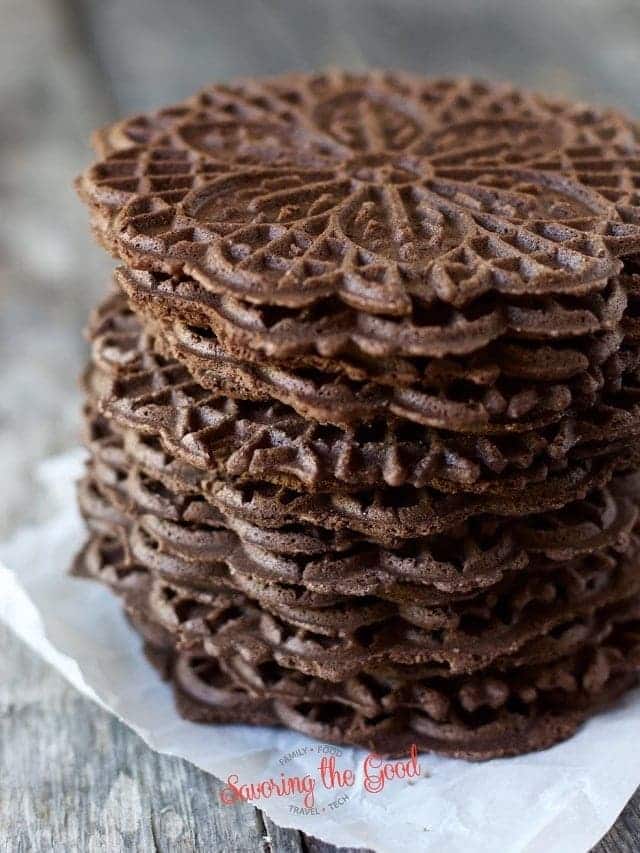 A stack of chocolate pizzelle cookies on a piece of paper.